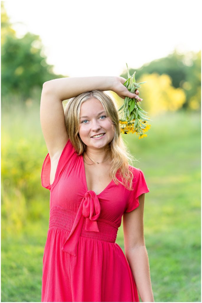 Senior girl wearing a pink dress poses in a wildflower field for her senior picture session in Columbia, Missouri by West Plains, Missouri photographer, Hannah Carr Photography