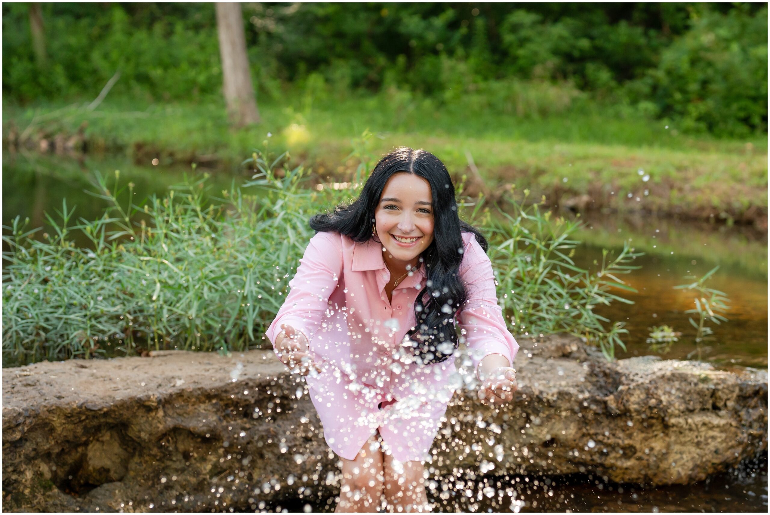 Highland High School senior, Dacy-Lynn, splashes water towards the camera in a creek in beautiful Cherokee Village, AR for her senior session with North Arkansas Senior Photographer, Hannah Carr Photography.